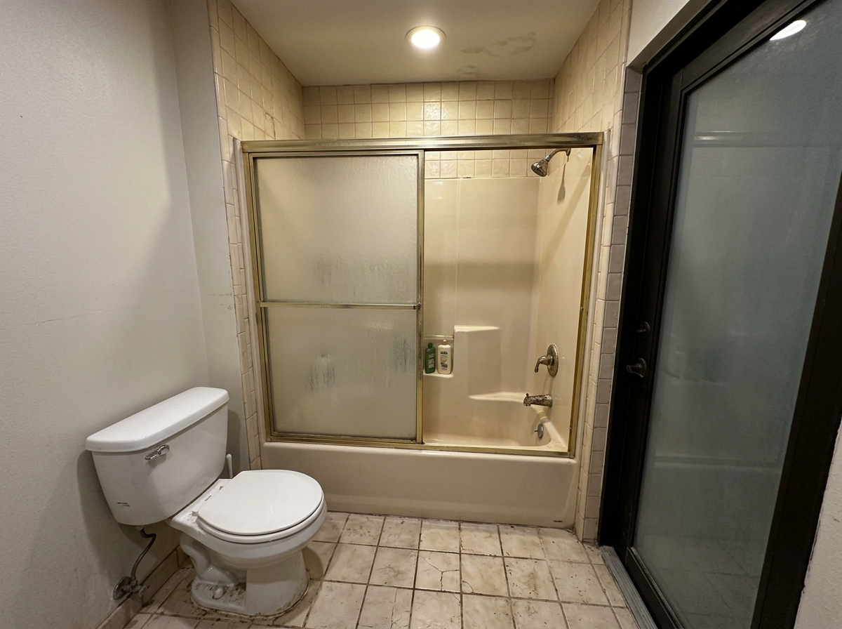 Same bathroom before — dated tub-shower and beige tile